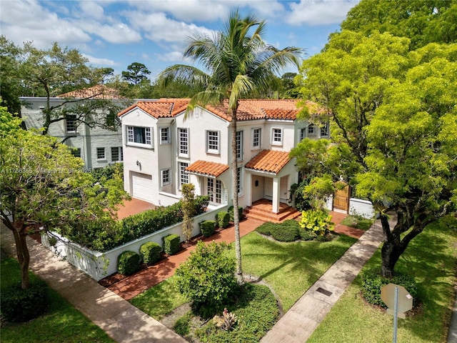 mediterranean / spanish-style house featuring a tile roof, stucco siding, an attached garage, fence, and a front lawn