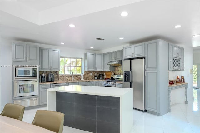 kitchen featuring a warming drawer, gray cabinets, decorative backsplash, a sink, and appliances with stainless steel finishes