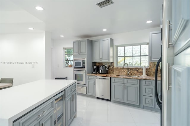 kitchen with decorative backsplash, a sink, gray cabinets, and appliances with stainless steel finishes