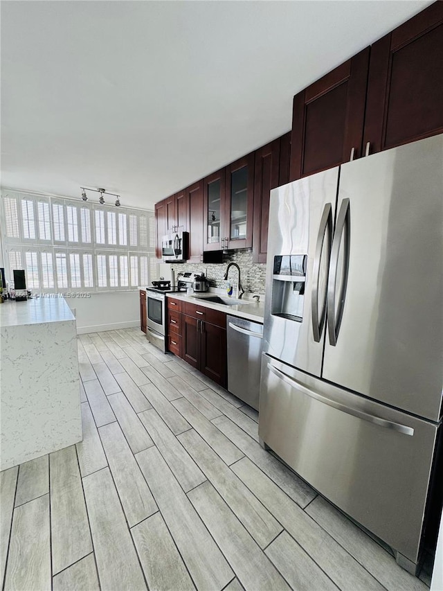 kitchen with light countertops, a sink, appliances with stainless steel finishes, glass insert cabinets, and decorative backsplash