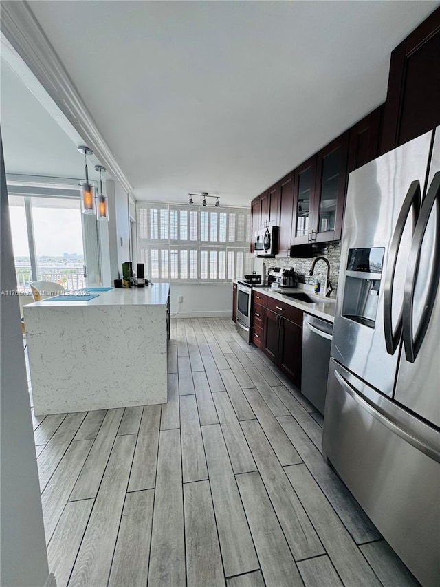 kitchen featuring light countertops, a sink, glass insert cabinets, wood finish floors, and stainless steel appliances