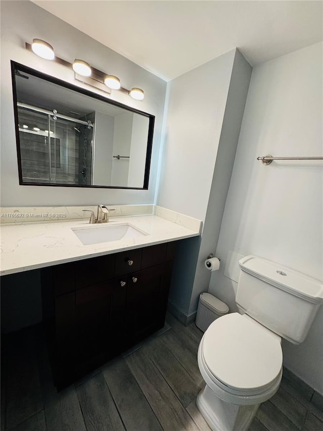 full bath featuring toilet, vanity, a shower stall, and wood finished floors