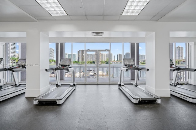 workout area featuring a city view, baseboards, and a paneled ceiling