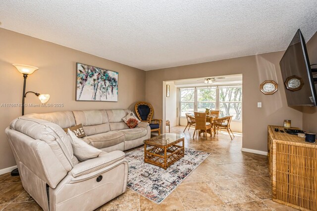 living area with ceiling fan, a textured ceiling, and baseboards