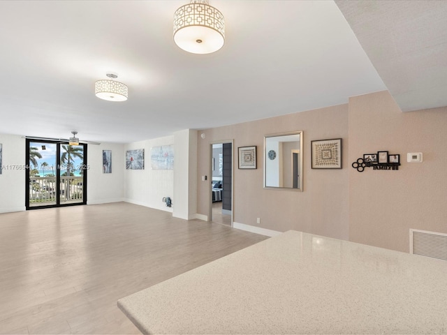 unfurnished room with baseboards, visible vents, ceiling fan, expansive windows, and light wood-type flooring