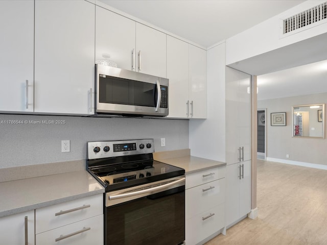 kitchen with light wood-type flooring, visible vents, white cabinetry, appliances with stainless steel finishes, and light countertops