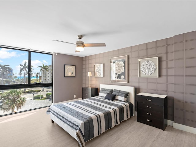bedroom featuring light wood finished floors, a ceiling fan, a wall of windows, and baseboards
