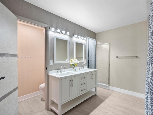 bathroom with toilet, wood finished floors, a stall shower, and a sink