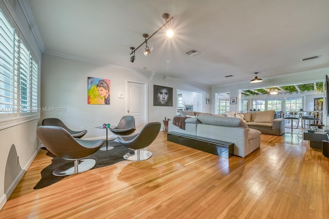 living area with wood-type flooring, ornamental molding, baseboards, and visible vents