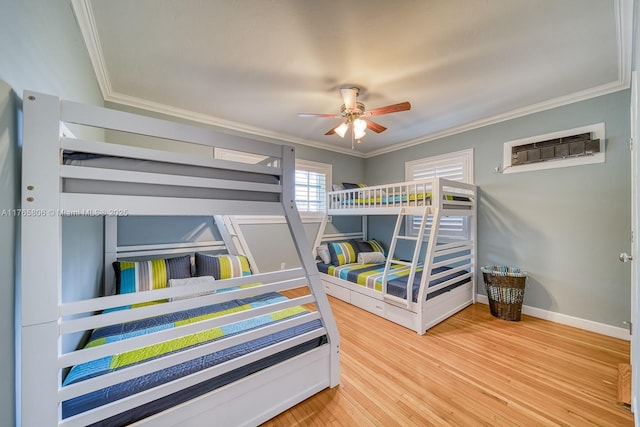 bedroom with a wall mounted AC, ornamental molding, baseboards, a ceiling fan, and wood finished floors