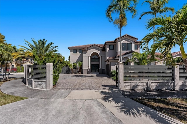 mediterranean / spanish-style house featuring a fenced front yard, stucco siding, a tile roof, and a gate