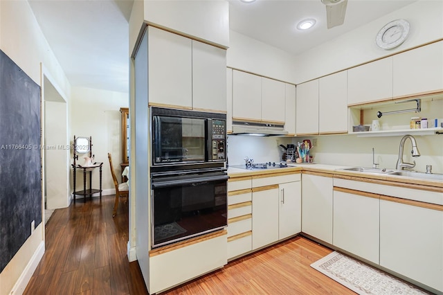 kitchen featuring under cabinet range hood, light wood-type flooring, light countertops, black appliances, and a sink
