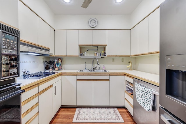 kitchen featuring light wood finished floors, a sink, stainless steel appliances, light countertops, and under cabinet range hood