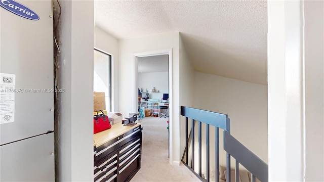 hallway with an upstairs landing, a textured ceiling, and carpet flooring