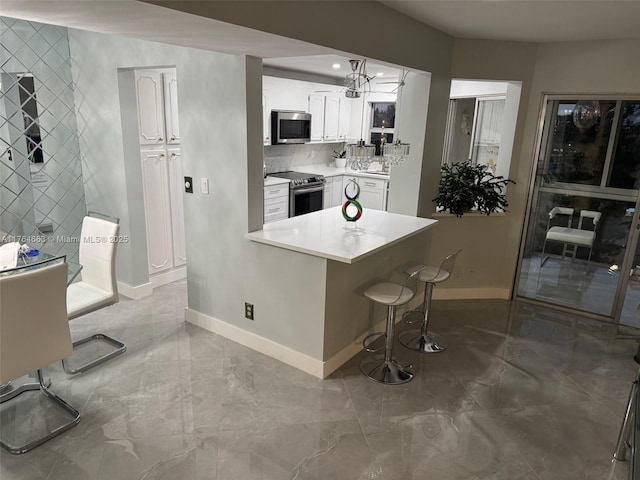 kitchen featuring white cabinets, appliances with stainless steel finishes, a breakfast bar area, marble finish floor, and baseboards