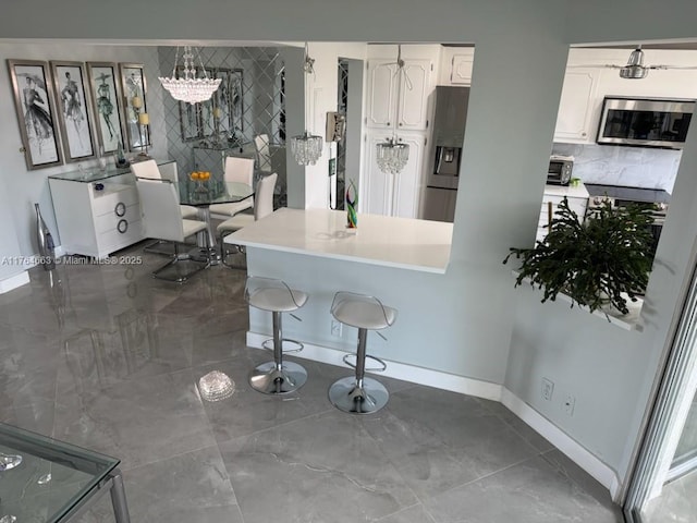 kitchen with baseboards, white cabinets, a breakfast bar area, and appliances with stainless steel finishes