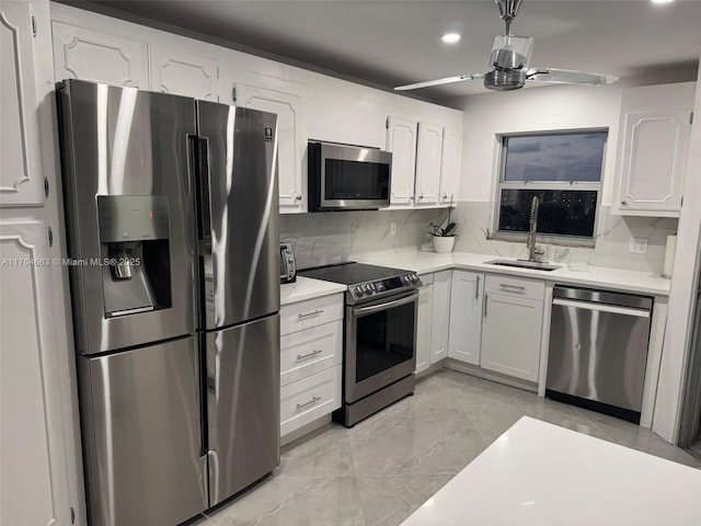 kitchen with a sink, stainless steel appliances, light countertops, a ceiling fan, and white cabinets