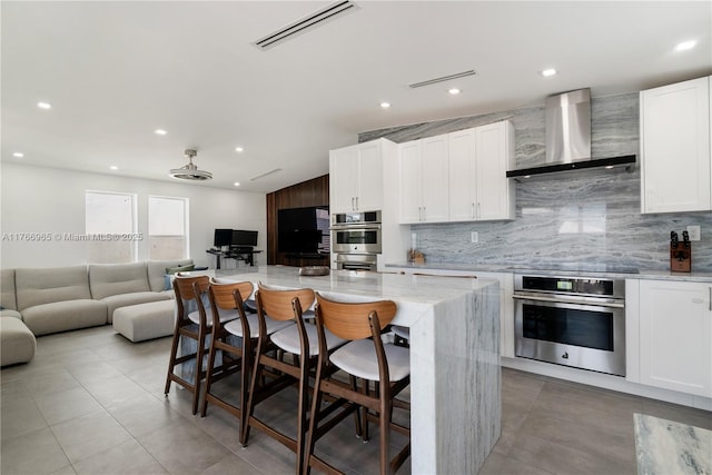 kitchen with visible vents, open floor plan, stainless steel double oven, wall chimney range hood, and black electric cooktop