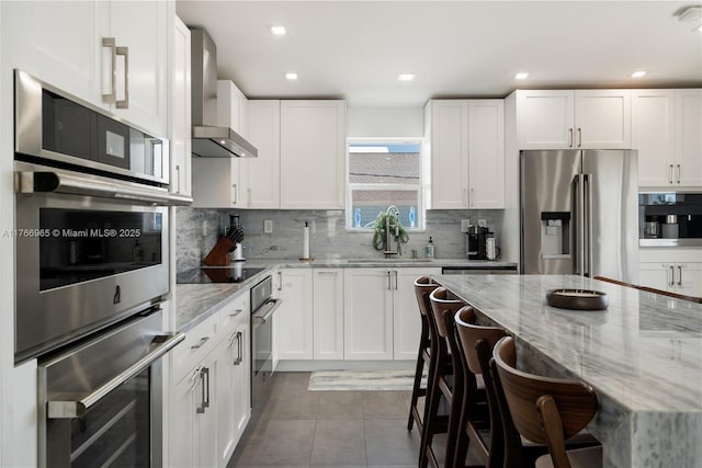 kitchen featuring light stone countertops, a breakfast bar, a sink, wall chimney range hood, and stainless steel fridge