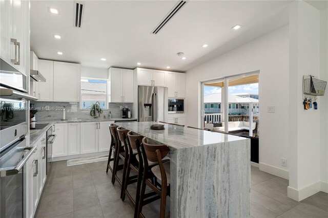 kitchen with light stone countertops, visible vents, stainless steel fridge with ice dispenser, decorative backsplash, and a center island