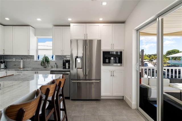 kitchen with backsplash, light stone counters, light tile patterned floors, stainless steel appliances, and white cabinetry