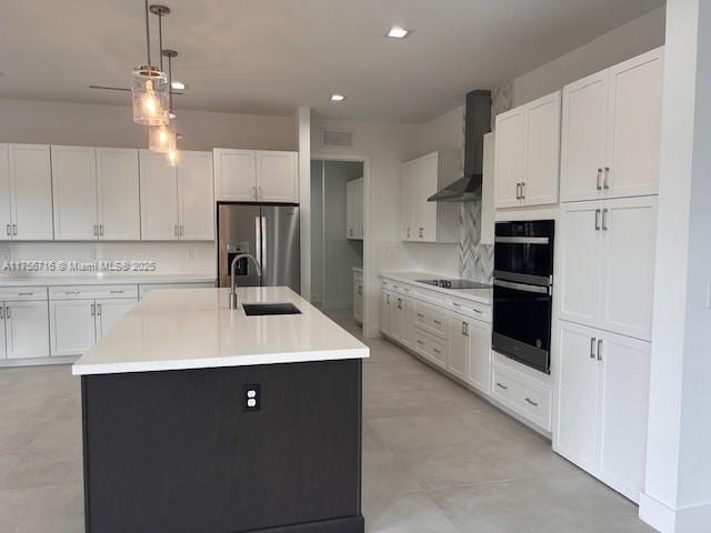 kitchen with wall chimney range hood, white cabinets, a sink, and black appliances
