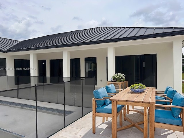 rear view of property featuring a standing seam roof, stucco siding, a patio, metal roof, and outdoor dining space