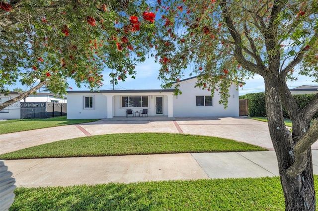 ranch-style house with a front lawn, concrete driveway, fence, and stucco siding