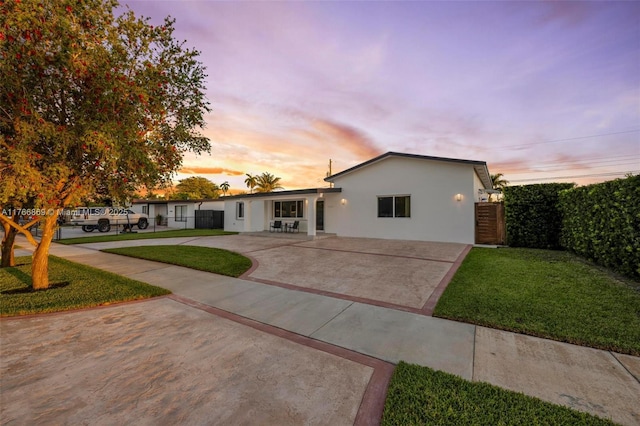 ranch-style house featuring fence, stucco siding, concrete driveway, a patio area, and a lawn