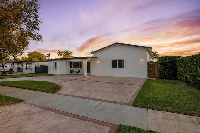 ranch-style home with curved driveway, fence, a lawn, stucco siding, and a patio area