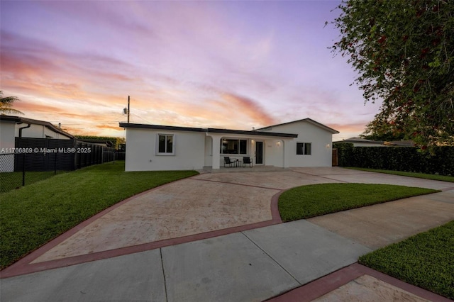 view of front of house featuring fence, stucco siding, a yard, a patio area, and driveway