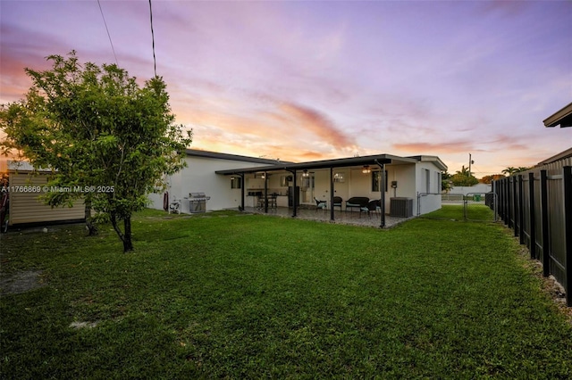 back of house at dusk featuring a gate, fence, a yard, central AC unit, and a patio area
