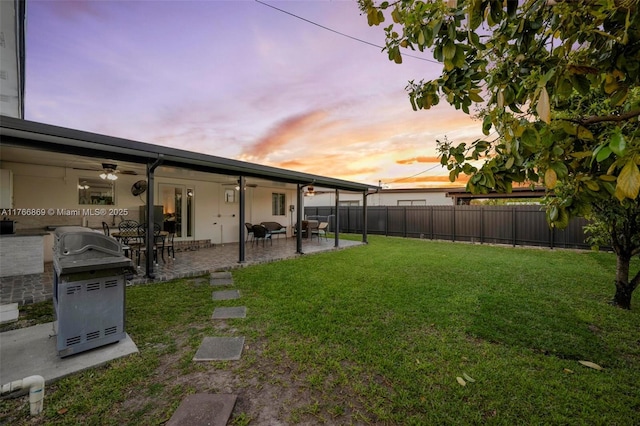 yard at dusk featuring a patio area, ceiling fan, and a fenced backyard