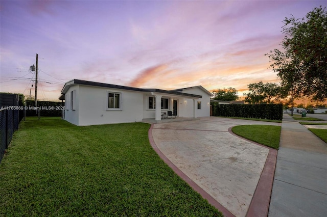 view of front of house with stucco siding, curved driveway, a yard, and fence