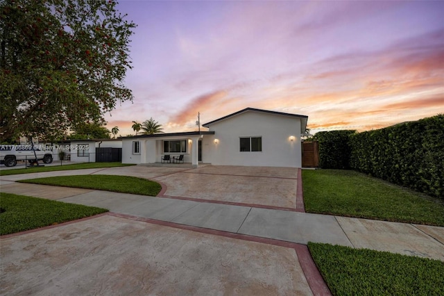 view of front of home with stucco siding, a lawn, a patio, fence, and concrete driveway