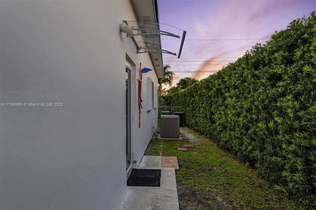 property exterior at dusk featuring stucco siding, central AC unit, and fence