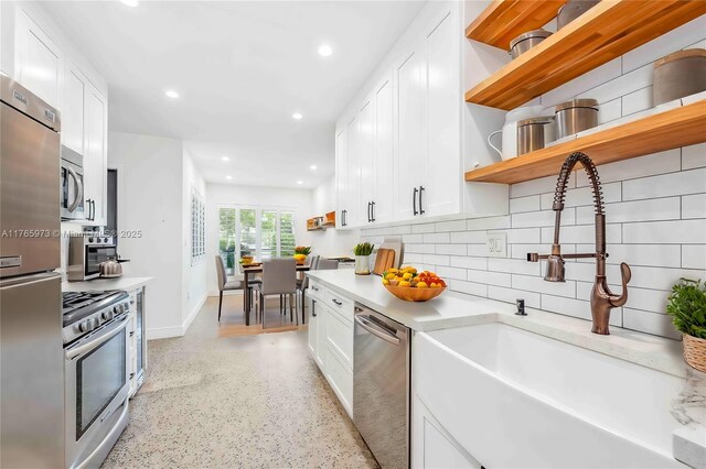 kitchen featuring open shelves, light countertops, white cabinetry, a sink, and stainless steel appliances