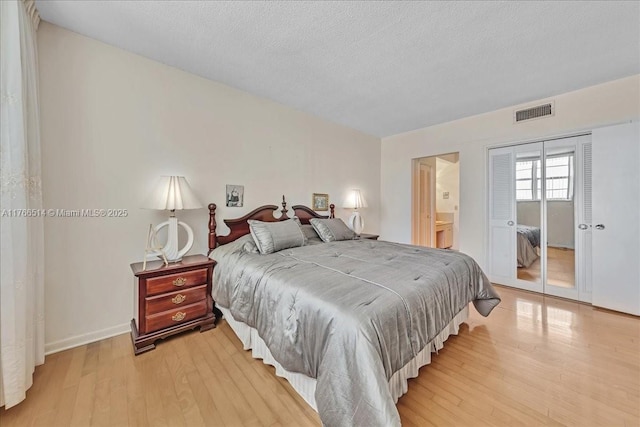 bedroom featuring visible vents, a textured ceiling, a closet, light wood-style floors, and baseboards