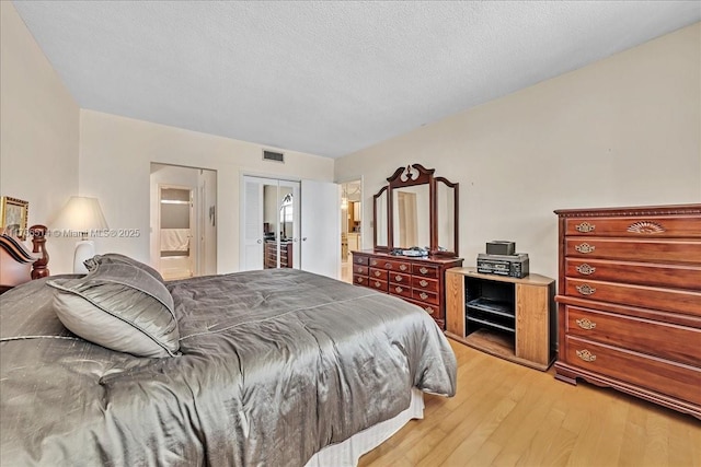 bedroom with light wood finished floors, visible vents, connected bathroom, and a textured ceiling