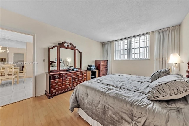 bedroom with light wood-style flooring, a textured ceiling, and an inviting chandelier