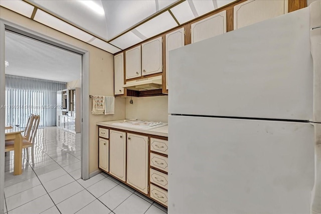 kitchen with under cabinet range hood, white appliances, light tile patterned floors, and light countertops