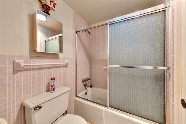 full bath with a wainscoted wall, tile walls, toilet, and combined bath / shower with glass door