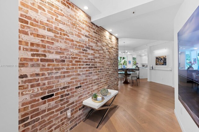 corridor featuring baseboards, wood finished floors, and brick wall