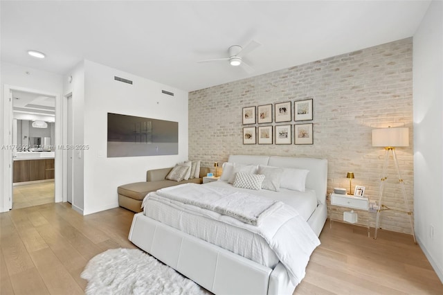 bedroom with visible vents, baseboards, wood finished floors, and brick wall
