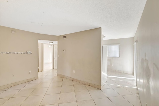 empty room with a textured ceiling, visible vents, baseboards, ceiling fan, and light tile patterned floors