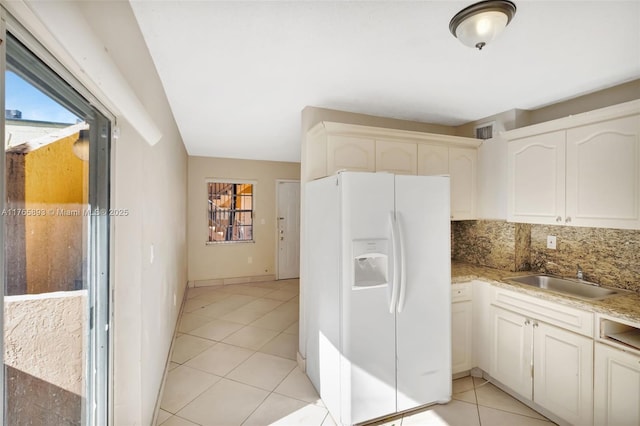 kitchen featuring white refrigerator with ice dispenser, backsplash, a sink, light tile patterned flooring, and visible vents