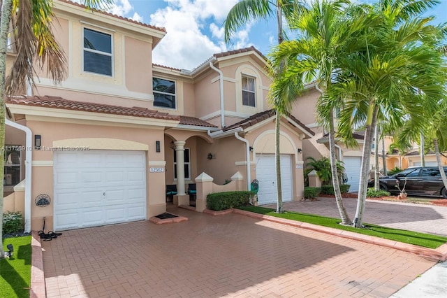 mediterranean / spanish-style home with a garage, decorative driveway, a tile roof, and stucco siding