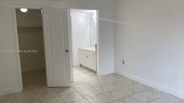 5102 NW 79th Ave Unit 304, Doral, FL 33166 - unfurnished bedroom featuring light tile patterned floors, connected bathroom, baseboards, and a walk in closet
