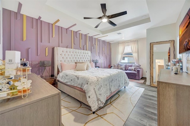 bedroom with light wood-style flooring, baseboards, a raised ceiling, and ceiling fan