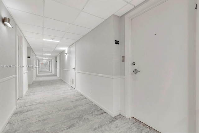 corridor with a paneled ceiling and light wood-type flooring